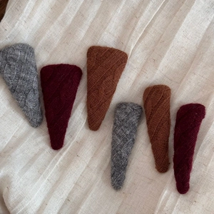 Close-up of six knitted triangle hair clips in grey, burgundy and brown cable knit texture