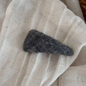 Detailed view of dark grey knitted triangle hair clip with textured cable knit pattern