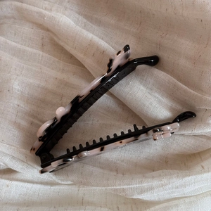 Detailed close-up of pink and black marble pattern acetate banana hair clip on beige fabric