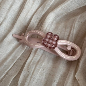 Détail de la pince à cheveux lapin rose avec motif à carreaux sur tissu en lin beige