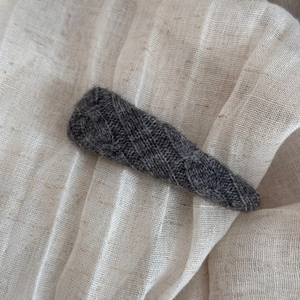 Close-up of a dark grey knitted triangle hair clip with retro cable knit texture