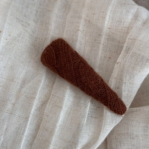 Close-up of a brown knitted triangular hair clip with fine twill texture on linen