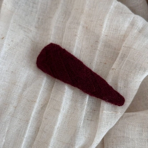 Detailed close-up of dark red knitted hair clip texture on a rustic linen background