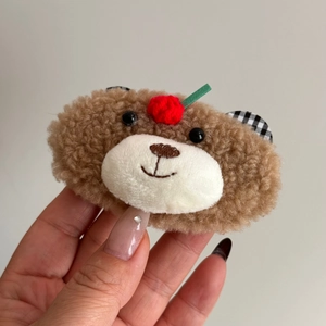 Détail de la pince à cheveux en peluche ours brun avec petit fruit rouge tricoté
