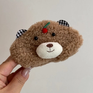 Détail d'une pince à cheveux en peluche ours marron avec cerise rouge et oreilles à carreaux