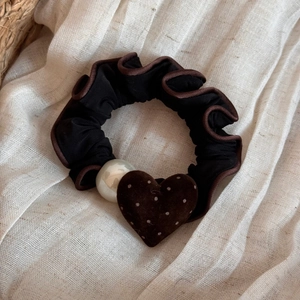 Dettaglio dello scrunchie in pizzo nero con perla bianca e ciondolo a cuore con pois