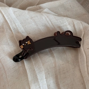 Detail of a shiny black resin banana hair clip featuring a cute cat design with gold whiskers