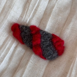 Détail d'une pince à cheveux artisanale en feutre de laine rayée rouge et grise pour l'hiver