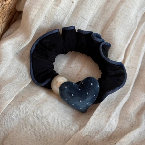 Dettaglio dell'elastico nero con pizzo blu, perla bianca e ciondolo a cuore a pois