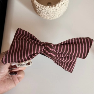 Detail of a large pink and brown striped fabric bow hair clip with a small fabric brand tag