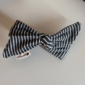 Detailed close-up of a striped fabric bow hair clip with a brand woven label and soft texture