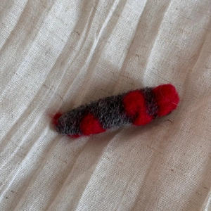 Détail de la pince à cheveux en feutre de laine avec pois rouges sur tissu gris doux