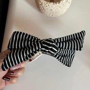 Close-up of black and white striped fabric bow hair clip with a woven brand tag detail