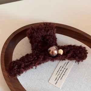 Detail of plush brown claw clip with a refined metallic gold emblem and central copper bead