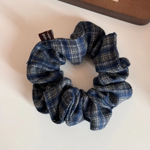 Detail shot of a blue and grey plaid fabric scrunchie with a premium woven brand label