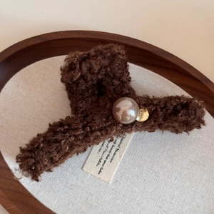 Close-up of brown plush shark hair claw with champagne pearl and gold metal tag
