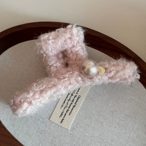 Detail of pink plush claw clip featuring a large faux pearl and a gold metallic logo tag