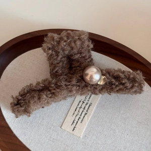 Detail of elegant brown plush hair claw with large pearl and gold metallic letter charm
