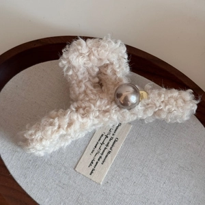 Detail of plush cream faux fur hair claw clip with metallic silver ball and gold emblem