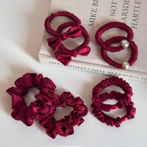 Set of 8 festive wine red satin scrunchies and bow hair ties for women on soft background