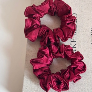 Close-up of two wine red satin scrunchies with elastic pleated fabric and silk-like luster