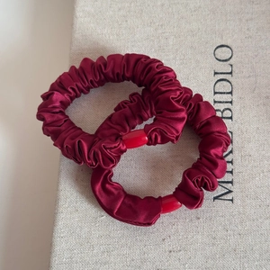 Close-up of two burgundy satin scrunchies with smooth red cylinder buckles on fabric