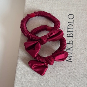 Detailed close-up of two wine red satin scrunchies with elegant bow knots on gift box
