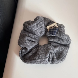 Dettaglio macro dell'elastico in maglia grigia con trecce e piccolo ciondolo a cuore