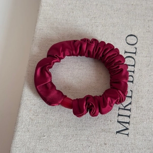 Close-up of a festive deep red satin scrunchie with smooth texture on a beige fabric box