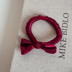 Detailed shot of dark red satin bow scrunchie with pleated texture on beige fabric