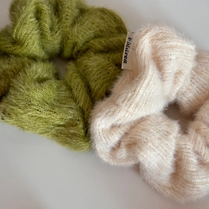 Dettaglio di elastici per capelli in maglia morbida verde e crema con etichetta logo