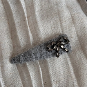 Détail de la pince à cheveux en peluche grise avec un nœud en strass étincelant