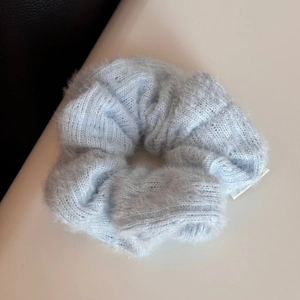 Dettaglio macro dell'elastico per capelli in maglia azzurra con texture morbida ed etichetta