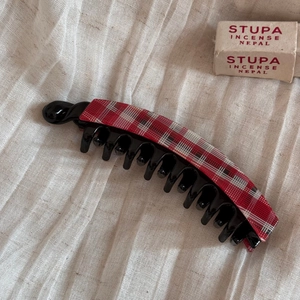 Detail of banana hair clip with red and white plaid fabric on a beige linen background