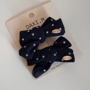 Detail of two navy blue polka dot bow hair clips with MAKE A WISH gold charms