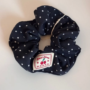 Detail view of navy blue polka dot scrunchie with a Sweet Cherry white woven fabric label