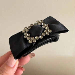 Detailed view of a black bow hair claw clip with a sparkling rectangular rhinestone accent