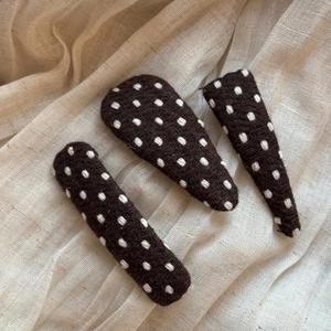 Close-up of three brown polka dot fabric hair clips on a soft beige linen background