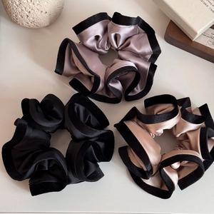 Détail de trois chouchous en satin bordés de velours en rose, noir et couleur champagne