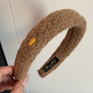 Detailed view of plush camel faux fur headband with a golden LOVE metal emblem