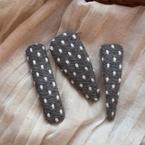 Close-up of three grey polka dot fabric BB hair clips on a soft textured background