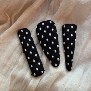 Detailed macro view of black fabric hair clips with white embroidered polka dots