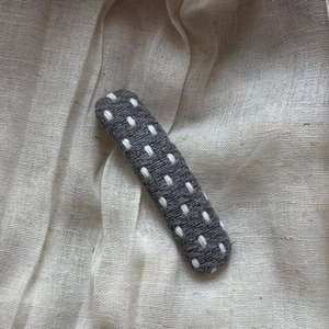 Close-up of dark grey polka dot fabric hair clip with white stitching on linen texture