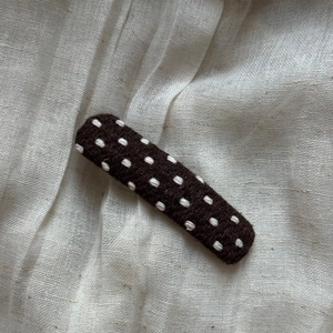 Detailed view of dark brown polka dot fabric hair clip on soft beige linen background