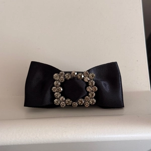 Detail of a black satin bow hair clip featuring a square rhinestone buckle for women