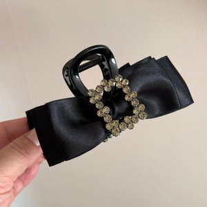 Close-up of black satin bow hair claw clip with elegant square rhinestone buckle detail
