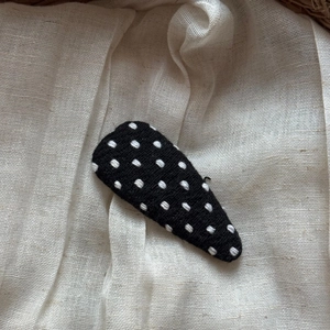 Close-up of fabric triangle hair clip with white polka dots on black textile background