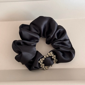 Detailed close-up of a black satin hair scrunchie with a sparkling heart rhinestone charm