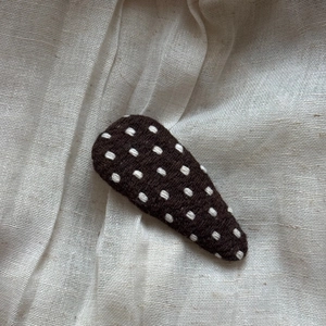 Close-up of handmade brown knitted triangle hair clip with white polka dot pattern detail