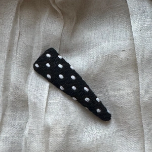 Close-up of a handmade black knit triangle hair clip with white polka dots